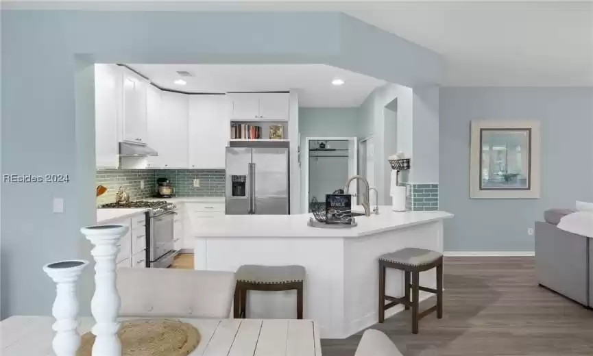 Kitchen featuring backsplash, light wood-type flooring, white cabinets, a breakfast bar area, and appliances with stainless steel finishes