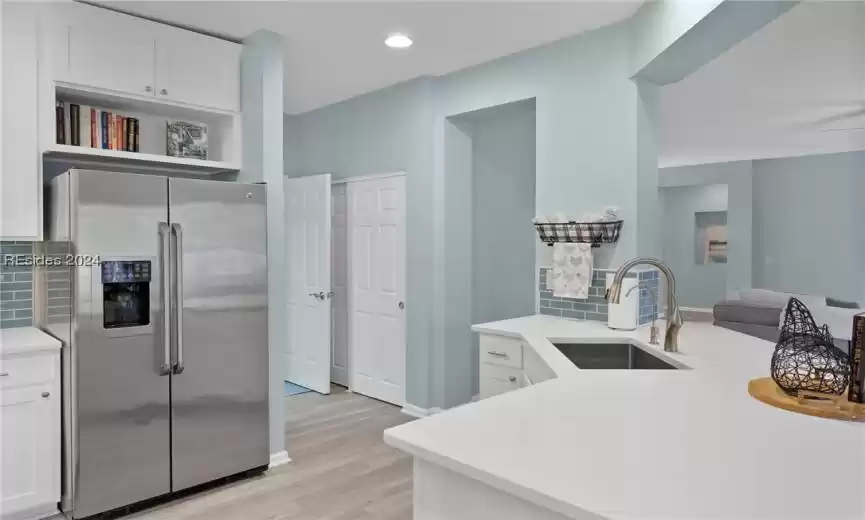 Kitchen featuring light wood-type flooring, high end refrigerator, white cabinetry, backsplash, and sink