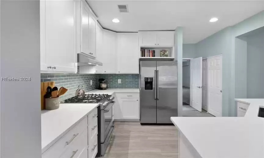 Kitchen featuring high end appliances, light hardwood / wood-style floors, backsplash, and white cabinetry