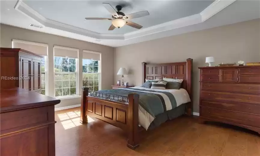 Bedroom featuring hardwood / wood-style flooring, ornamental molding, ceiling fan, and a raised ceiling