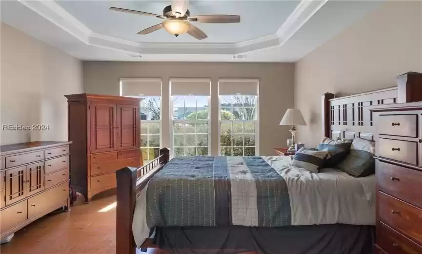 Bedroom with light wood-type flooring, a tray ceiling, ceiling fan, and ornamental molding