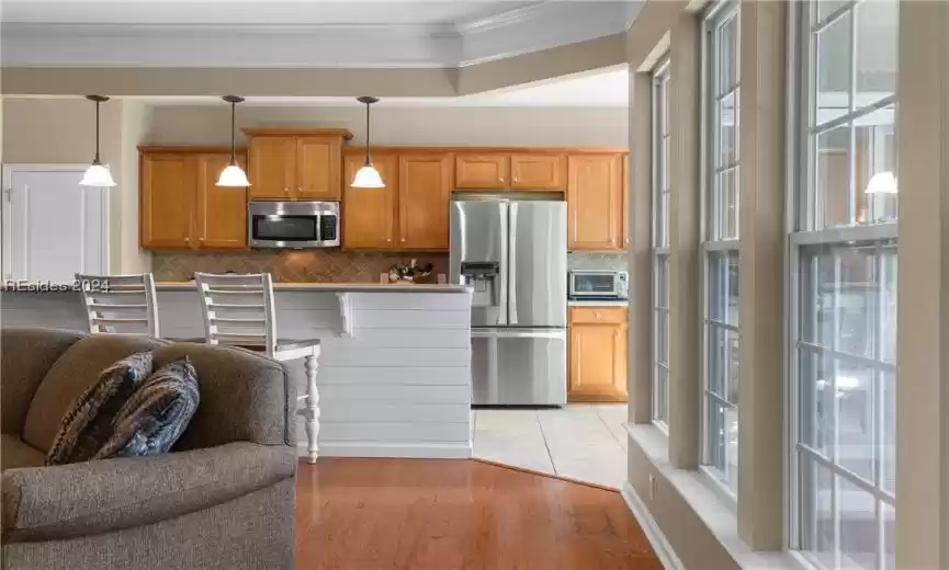 Kitchen featuring a raised ceiling, hanging light fixtures, crown molding, light tile floors, and appliances with stainless steel finishes
