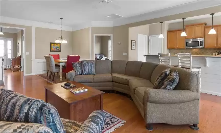 Living room featuring ceiling fan with notable chandelier, ornamental molding, and light wood-type flooring