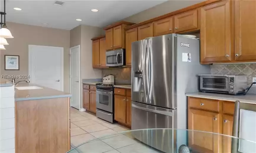 Kitchen with tasteful backsplash, sink, light tile floors, pendant lighting, and appliances with stainless steel finishes