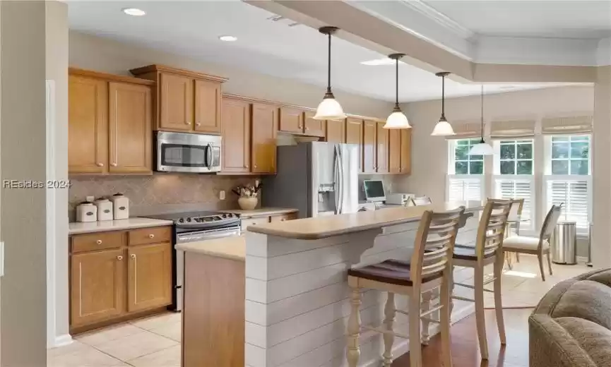 Kitchen featuring a kitchen island, a breakfast bar area, tasteful backsplash, decorative light fixtures, and appliances with stainless steel finishes