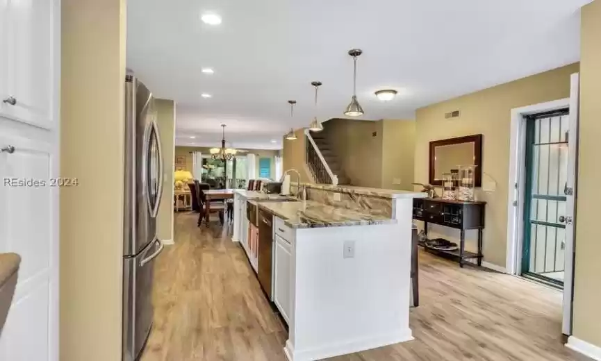 Kitchen with appliances with stainless steel finishes, hanging light fixtures, white cabinetry, and light hardwood / wood-style flooring