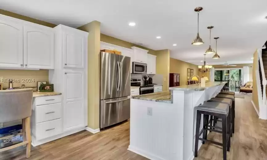 Kitchen with an island with sink, hanging light fixtures, white cabinets, light hardwood / wood-style floors, and stainless steel appliances