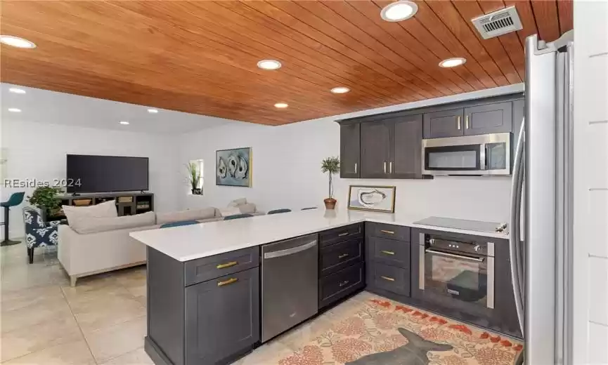 Kitchen with kitchen peninsula, light tile floors, stainless steel appliances, and wood ceiling