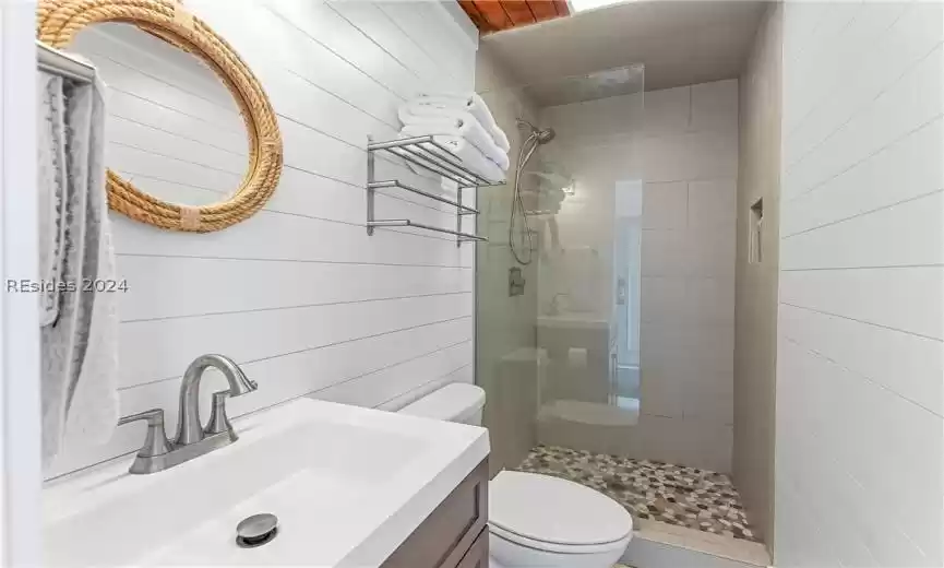 Bathroom with tiled shower, vanity, toilet, and wood walls