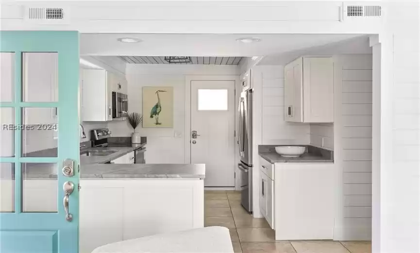 Kitchen featuring white cabinets, light tile floors, stainless steel appliances, and tasteful backsplash