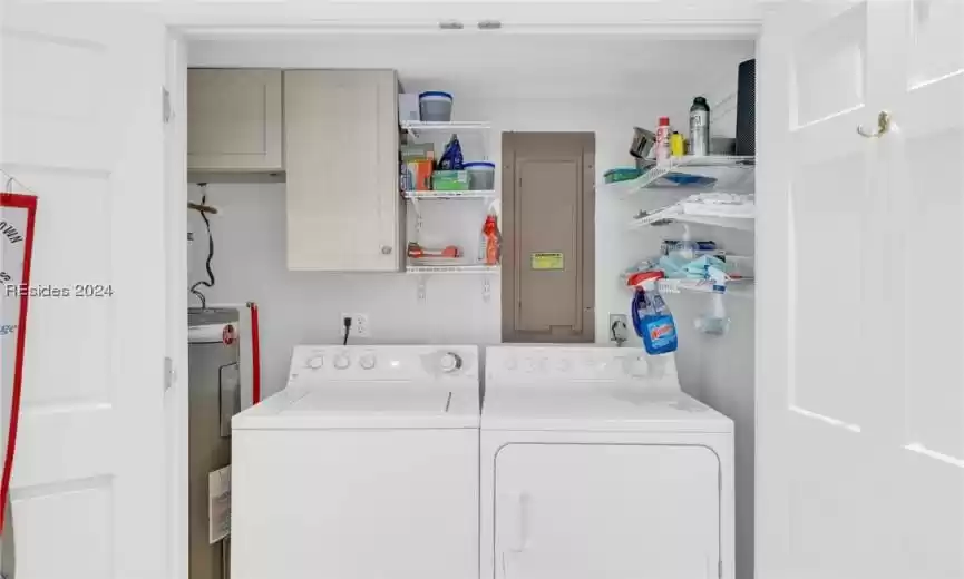 Laundry closet off of kitchen with washer and clothes dryer, electric water heater, and cabinets