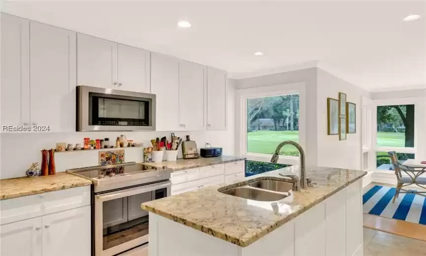 Kitchen featuring a center island with sink, backsplash, range with two ovens, stainless steel microwave, and sink