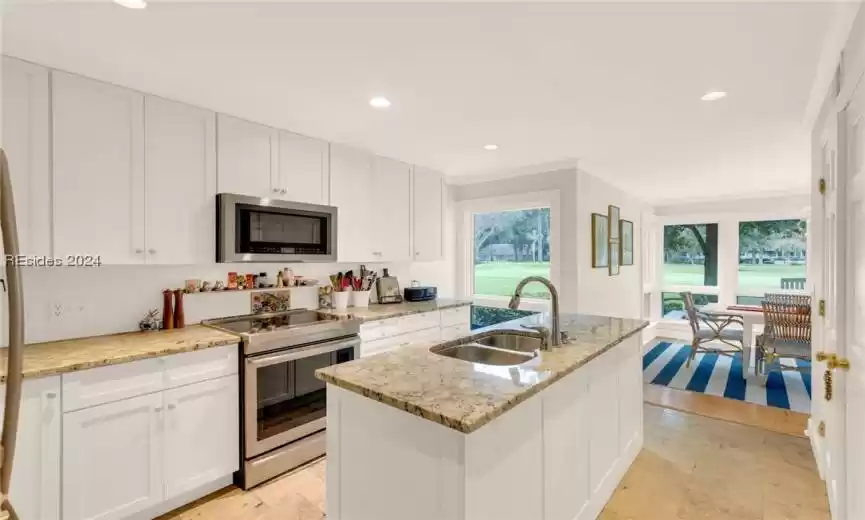 Kitchen featuring white cabinets, appliances with stainless steel finishes, a center island with sink, and backsplash