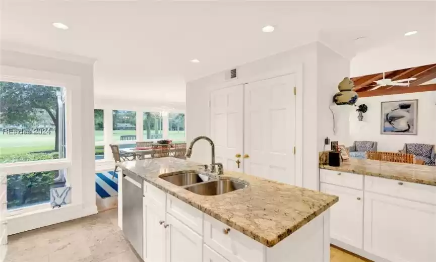 Kitchen with a center island with sink, light stone countertops, white cabinetry, sink, and light tile floors