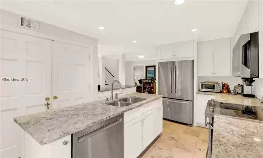Kitchen with stainless steel appliances, white cabinetry, light stone countertops, a kitchen island with sink, and sink