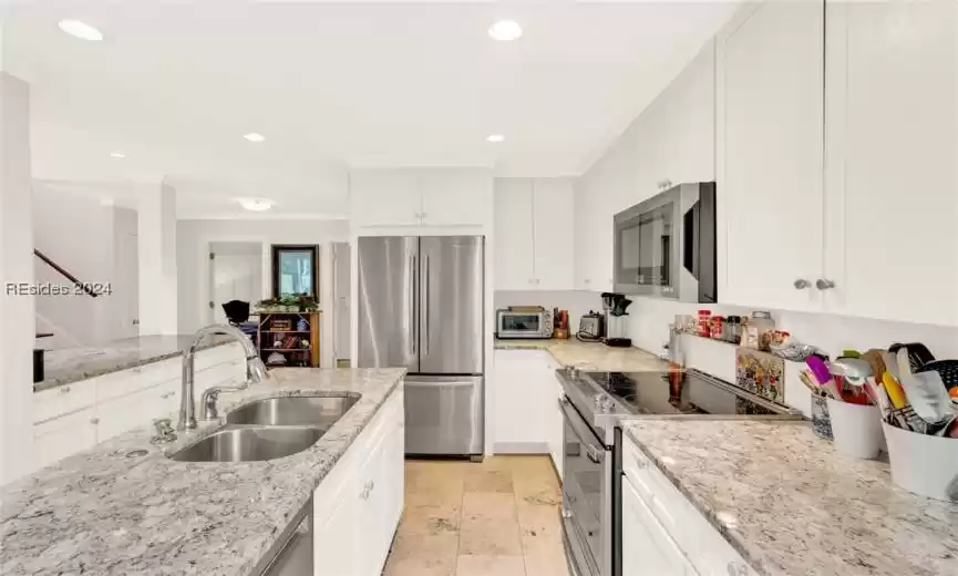Kitchen featuring stainless steel appliances, light stone counters, white cabinets, sink, and light tile floors