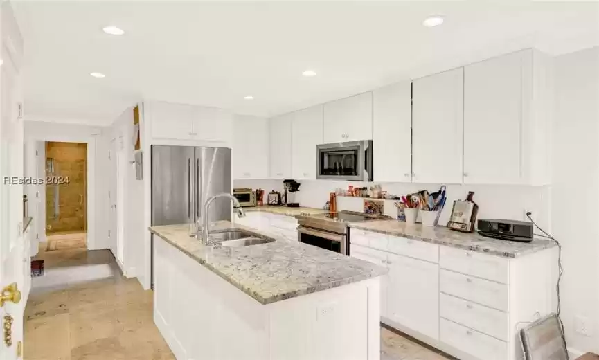Kitchen featuring white cabinets, sink, appliances with stainless steel finishes, and a center island with sink