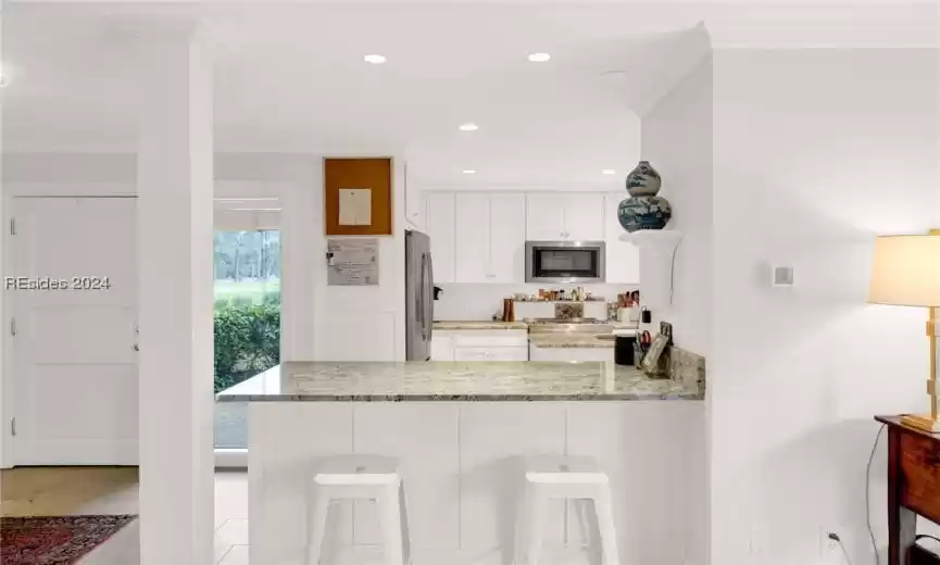 Kitchen with light stone counters, a kitchen breakfast bar, white cabinetry, kitchen peninsula, and appliances with stainless steel finishes