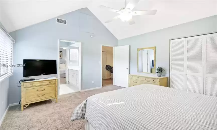 Carpeted bedroom with high vaulted ceiling, ceiling fan, connected bathroom, and a closet