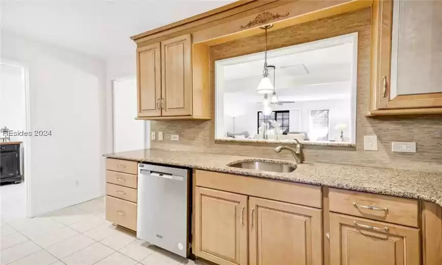 Kitchen featuring dishwasher, light stone counters, tasteful backsplash, sink, and decorative light fixtures