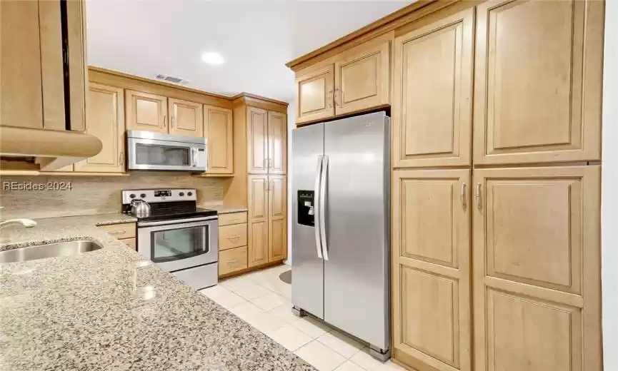 Kitchen featuring backsplash, light stone counters, sink, light tile floors, and stainless steel appliances