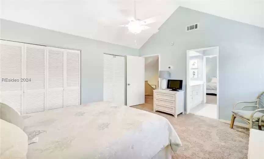 Tiled bedroom with multiple closets, ensuite bedroom with connected bath, ceiling fan, and high vaulted ceiling