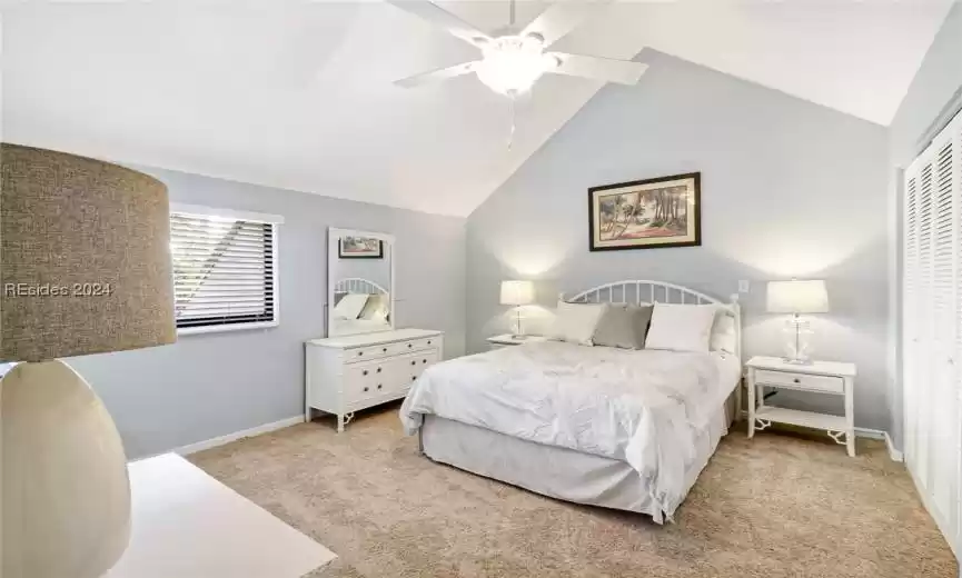 Guest Bedroom with a closet, light carpet, ceiling fan, and lofted ceiling