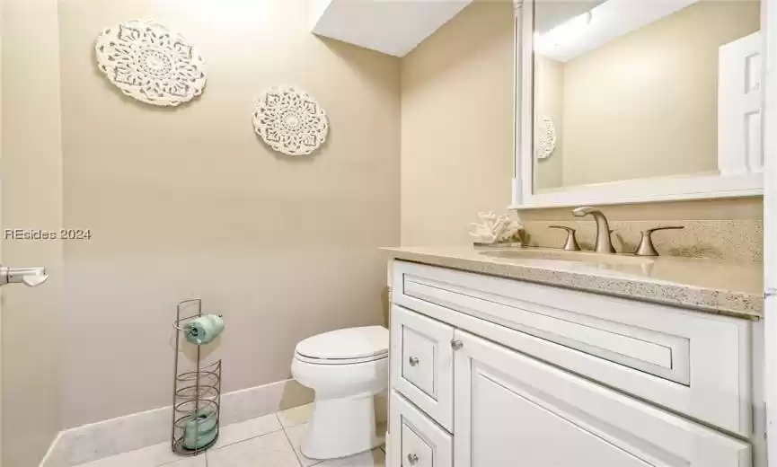 Hall (half) Bathroom for guests and convenience. 
 featuring vanity, tile flooring, and toilet