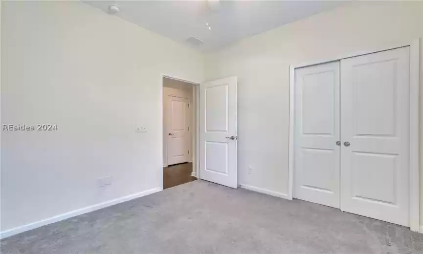 First floor guest room featuring light colored carpet, ceiling fan, and a large double doored closet