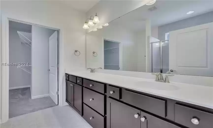 Primary bathroom featuring double sink, oversized vanity, a shower with door, and tile floors