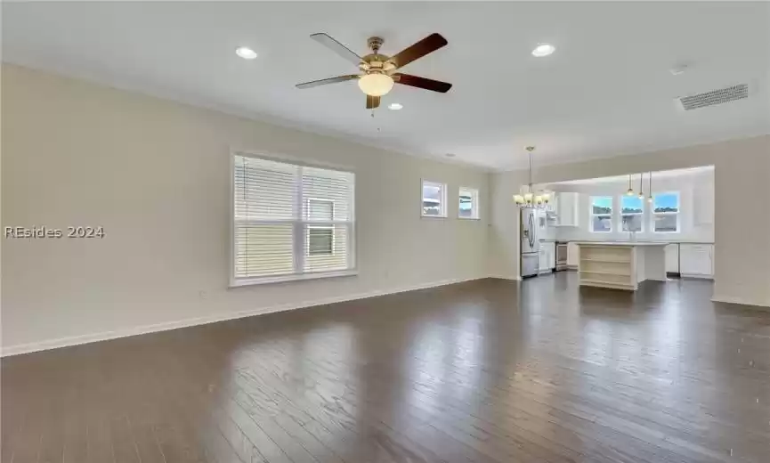 Living room features crown molding, ceiling fan with notable chandelier, a healthy amount of sunlight, and dark wood-type flooring