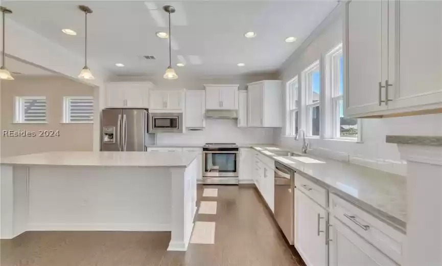 Kitchen with white cabinetry, backsplash, stainless steel appliances, and hardwood / wood-style floors