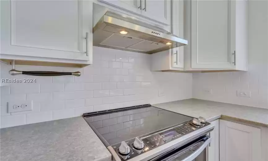 Kitchen with electric stove, white cabinetry, and tasteful backsplash