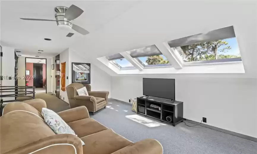Carpeted living room featuring ceiling fan and vaulted ceiling with skylight