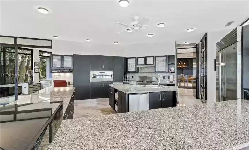 Kitchen featuring ceiling fan with notable chandelier, sink, an island with sink, appliances with stainless steel finishes, and light stone countertops