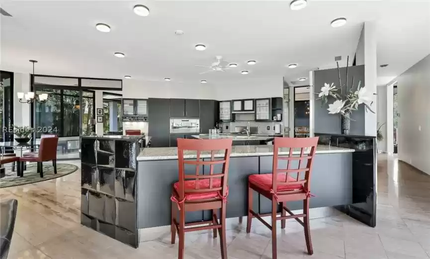 Kitchen featuring ceiling fan with notable chandelier, a breakfast bar, pendant lighting, wall oven, and light stone counters
