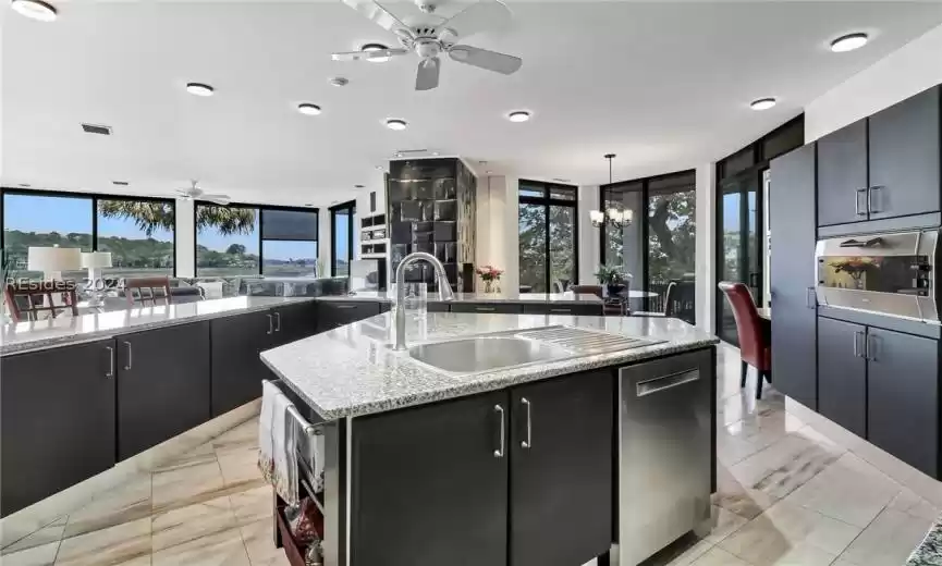 Kitchen featuring a kitchen island with sink, ceiling fan with notable chandelier, light tile floors, and decorative light fixtures