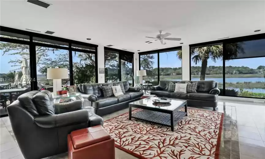 Living room featuring light tile flooring, floor to ceiling windows, ceiling fan, and a water view