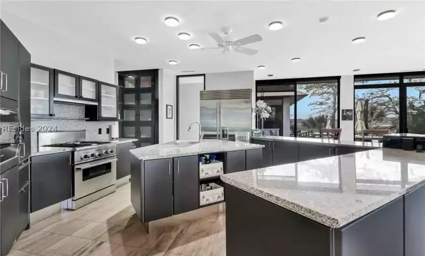 Kitchen featuring backsplash, a center island with sink, ceiling fan, premium appliances, and light stone countertops