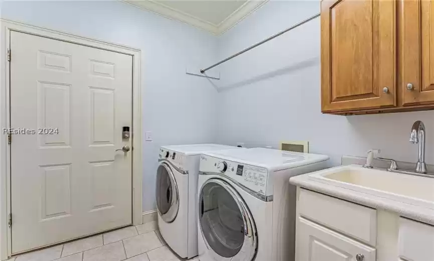 Clothes washing area featuring cabinets, sink, washer and clothes dryer, ornamental molding, and light tile floors