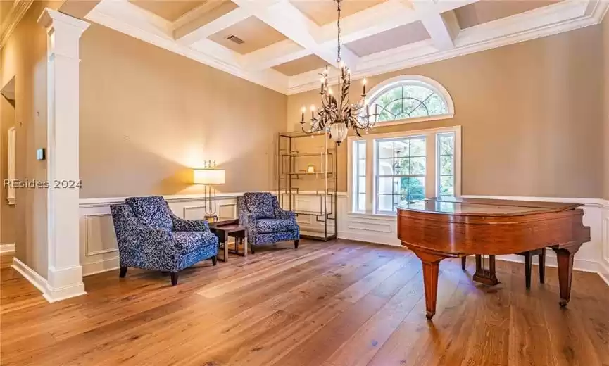 Sitting room with decorative columns, a notable chandelier, beam ceiling, coffered ceiling, and light wood-type flooring
