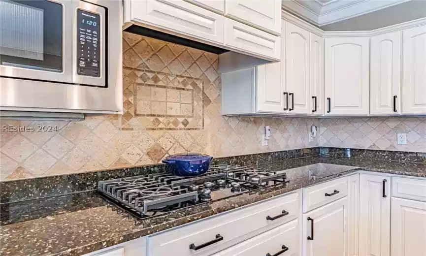Kitchen featuring backsplash, white cabinetry, and stainless steel microwave