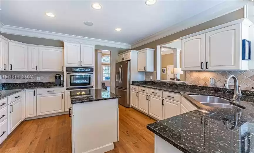 Kitchen featuring sink, white cabinets, backsplash, light hardwood / wood-style flooring, and stainless steel appliances