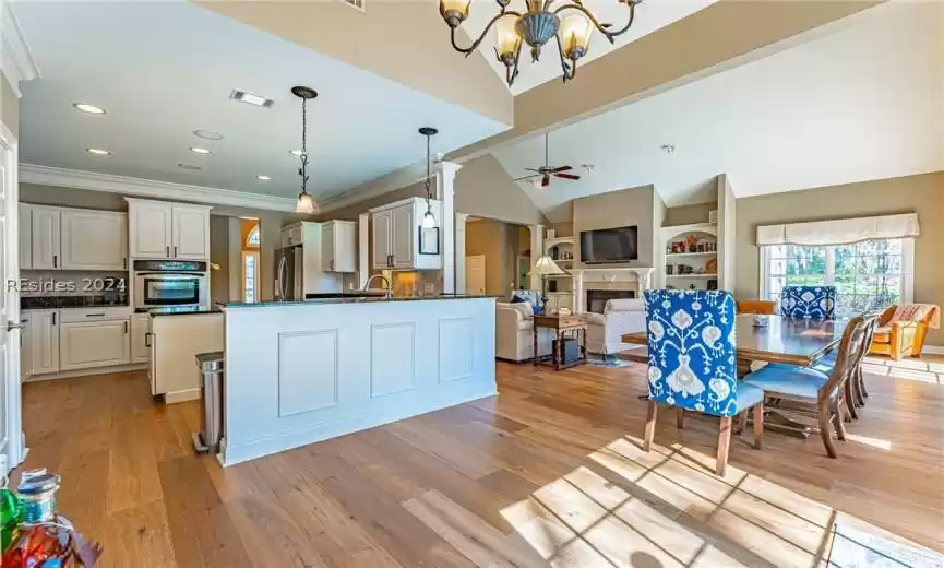 Kitchen featuring ceiling fan with notable chandelier, decorative light fixtures, a tiled fireplace, light wood flooring, and stainless steel appliances