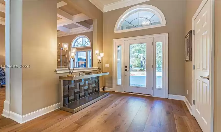 Entrance foyer with ornamental molding, beam ceiling, hardwood / wood floors, coffered ceiling, and a high ceiling