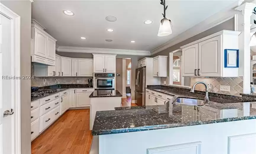 Kitchen featuring sink, dark stone countertops, backsplash, and light wood-type flooring