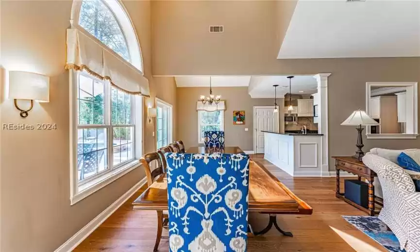 Dining area featuring a towering ceiling, decorative columns, a notable chandelier, sink, and dark hardwood / wood-style flooring