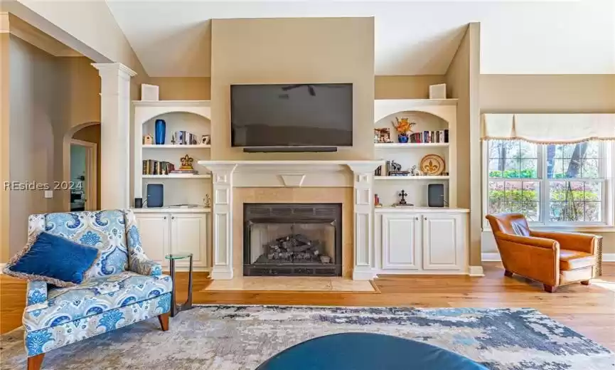 Living room featuring built in features, a fireplace, lofted ceiling, ornate columns, and light wood flooring