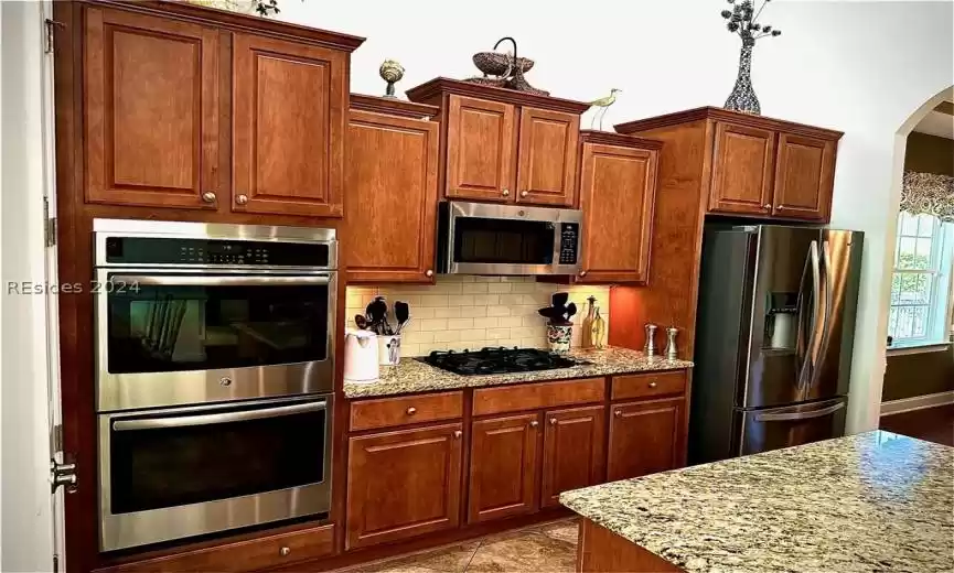 Kitchen with tasteful backsplash, appliances with stainless steel finishes, and light stone counters