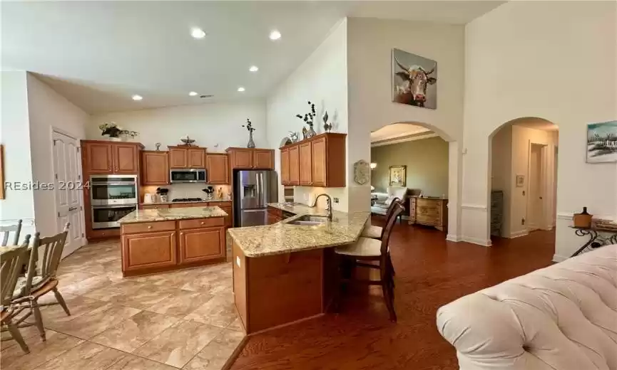 Kitchen with appliances with stainless steel finishes, a kitchen bar, sink, high vaulted ceiling, and light stone countertops